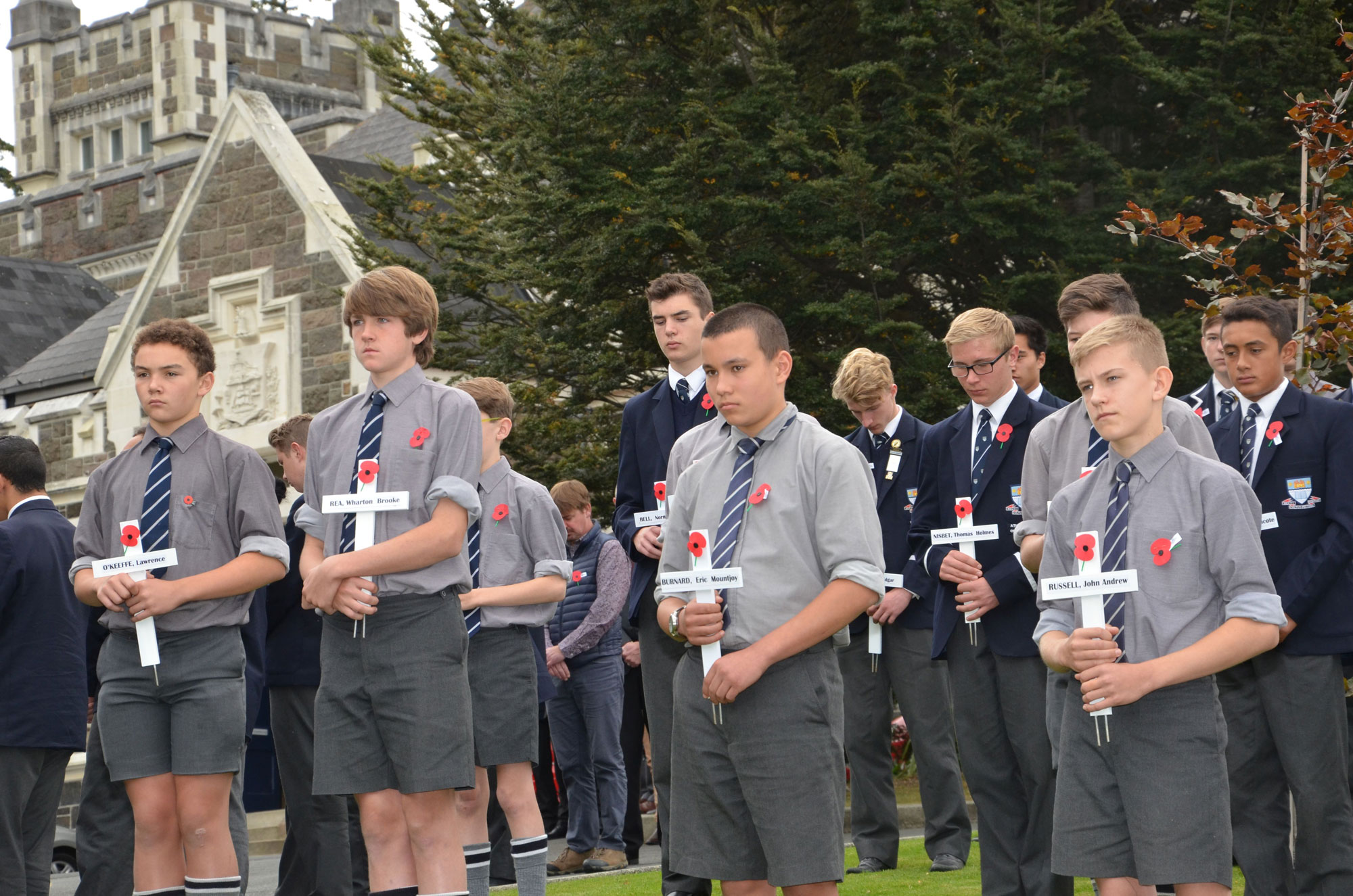 Otago Boys’ High School Students stand with white crosses and Anzac poppies to remember their fallen old boys